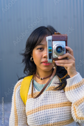 Portrait of a young Asian woman photographing with a vintage photo camera, vacation concept, covering half her face