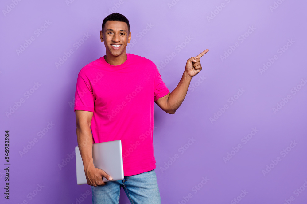 Portrait of nice positive satisfied man fade haircut pink t-shirt hold laptop directing empty space isolated on violet color background Portrait of nice positive satisfied man fade haircut pink t-shirt hold laptop directing empty space isolated on violet color background