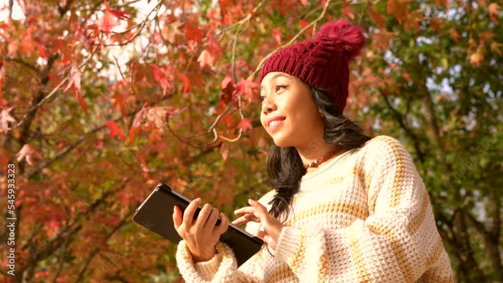 Asian girl in autumn with a tablet smiling in a forest of red leaves, technology concept Asian girl in autumn with a tablet smiling in a forest of red leaves, technology concept