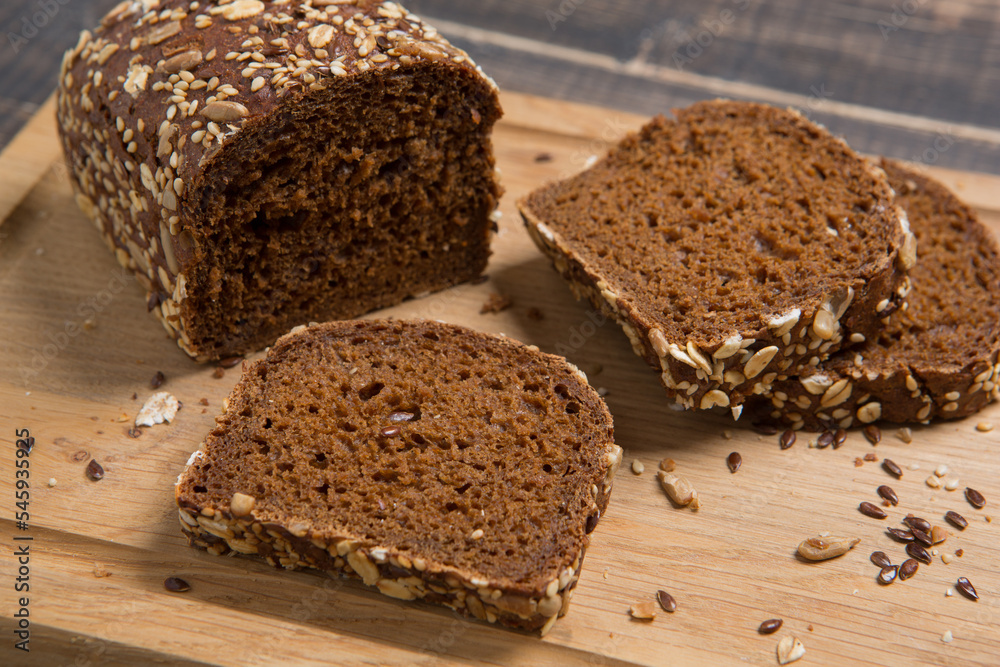 Loaf of brown bread, partially cut into pieces, with flax seeds, sunflower seeds and oatmeal, on a cutting board Loaf of brown bread, partially cut into pieces, with flax seeds, sunflower seeds and oatmeal, on a cutting board