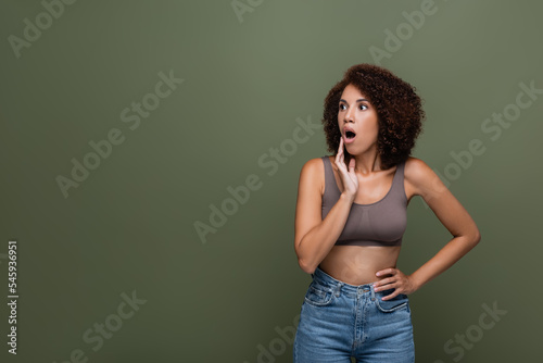Shocked african american woman in top holding hand on hip and looking away isolated on green. © LIGHTFIELD STUDIOS