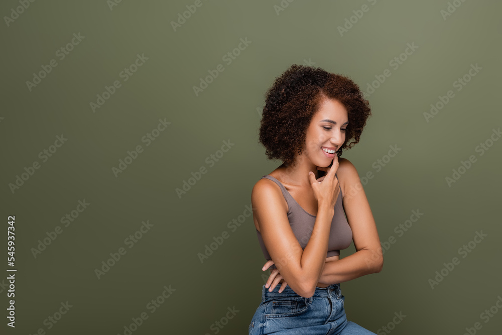 Positive african american woman in top touching chin isolated on green. Positive african american woman in top touching chin isolated on green.