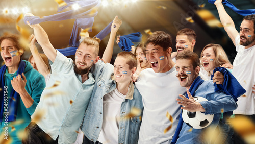 Принти на полотні Young emotive football fans from Argentina cheering national soccer team with blue scarfs at crowded stadium