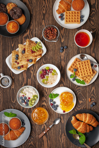 Continental breakfast. Top view. Flat lay. Coffee, tea, croissants, jam, egg, pancakes, maffins and oatmeal. Wooden background. Family breakfast table.
