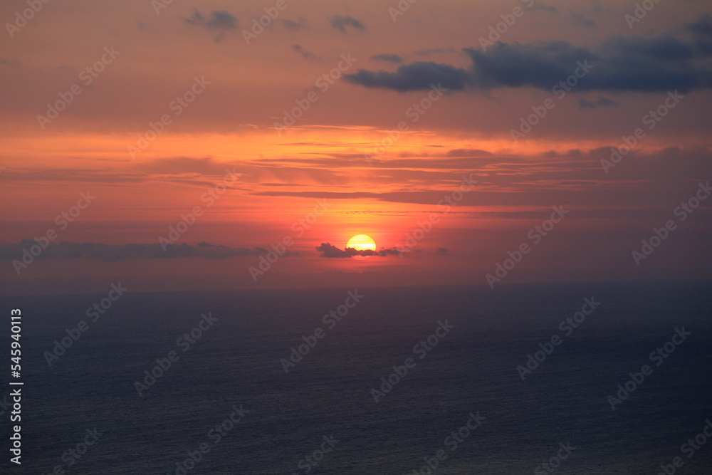 Orange sun over the sea in pink clouds in the evening light