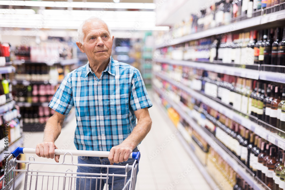 mature senor choosing alcoholic drinks in supermarket