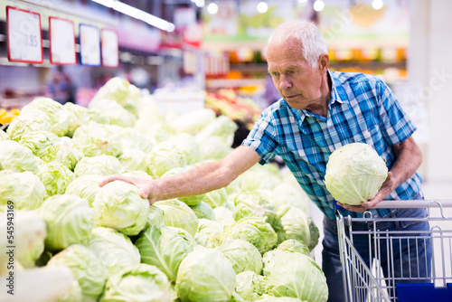 Mature senor examines cole in the vegetables section of supermarket photo