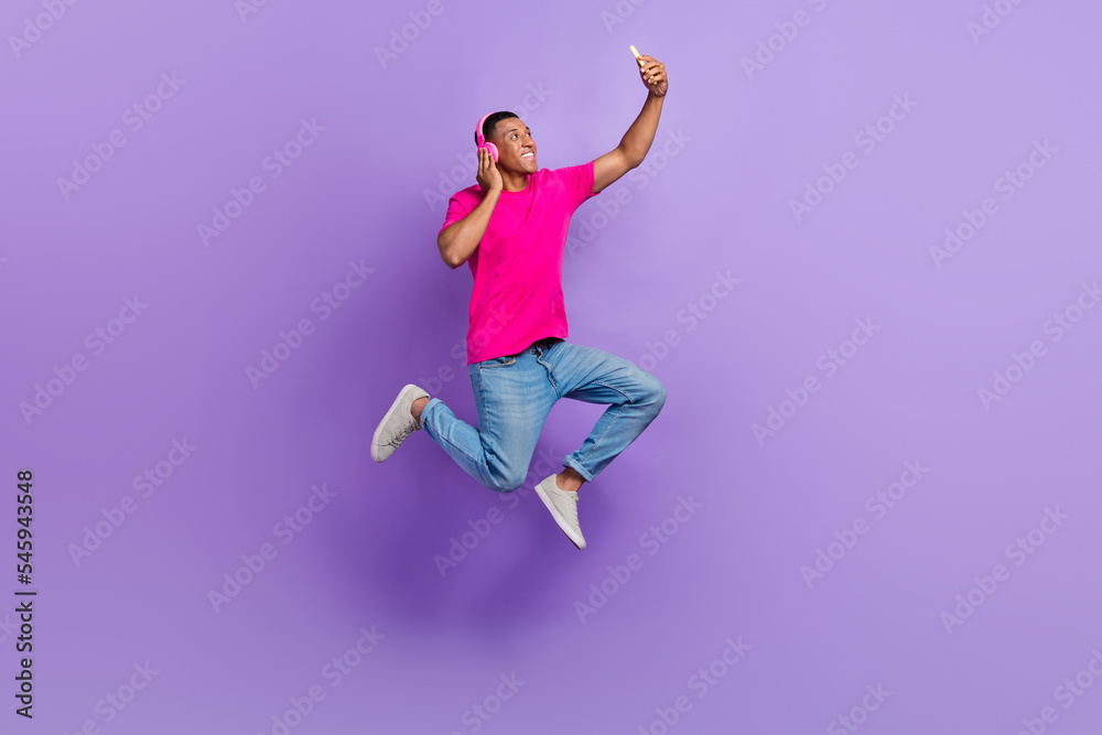 Full length photo of carefree handsome guy jumping hold telephone make selfie isolated on violet color background Full length photo of carefree handsome guy jumping hold telephone make selfie isolated on violet color background