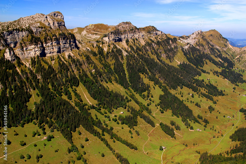 Landscape with the view of the mountain range, a hollow and houses in it against a blue sky with clouds on the mountain Niederhorn near Interlaken, Switzerland	