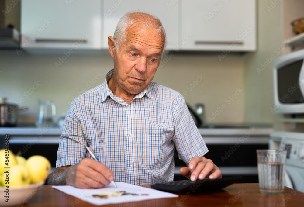 Elderly man sitting in kitchen and calculating money