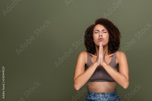 Curly african american woman with closed eyes praying isolated on green. © LIGHTFIELD STUDIOS