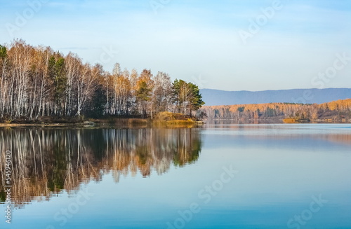 Autumn landscape on the lake with trees, mountains and sky with reflection in the water