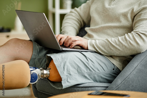 Close up of man with prosthetic leg using laptop while relaxing at home, copy space