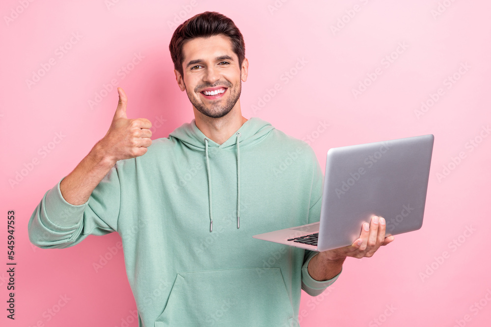 Photo of young positive successful video blogger hold laptop showing like thumb recommend new app for montage isolated on pink color background Photo of young positive successful video blogger hold laptop showing like thumb recommend new app for montage isolated on pink color background