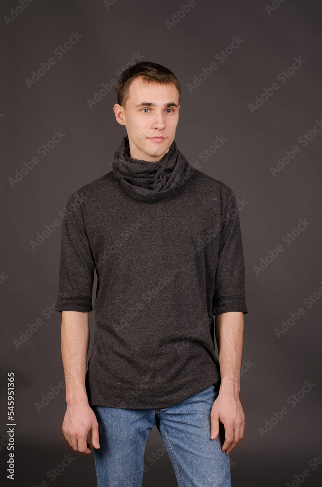 young man in a black sweater and jeans, on a studio gray background