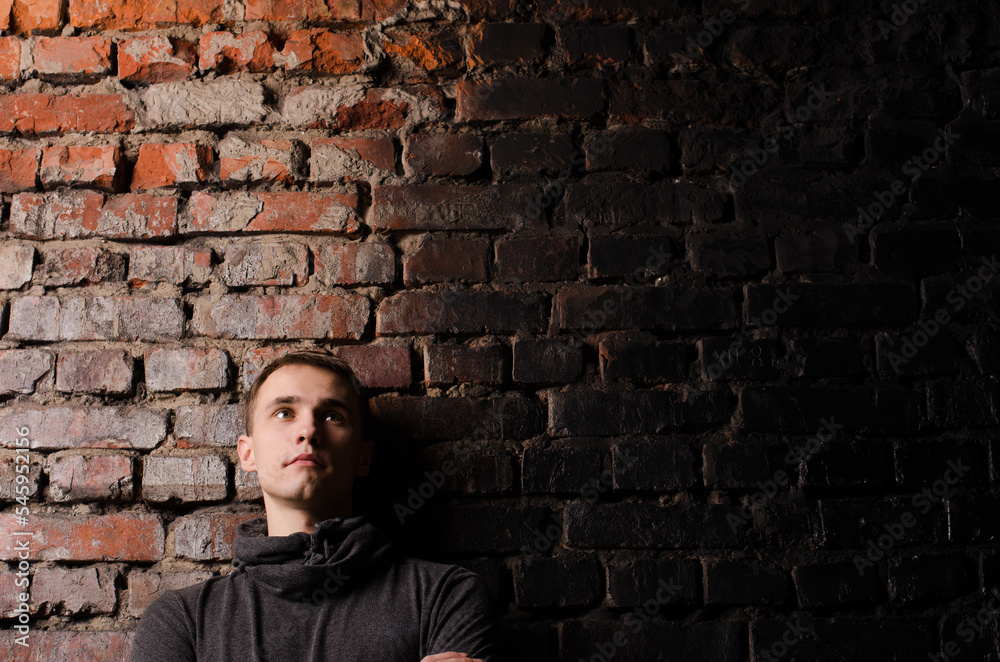 young man in a black jacket against the background of a brown, red and black brick wall young man in a black jacket against the background of a brown, red and black brick wall