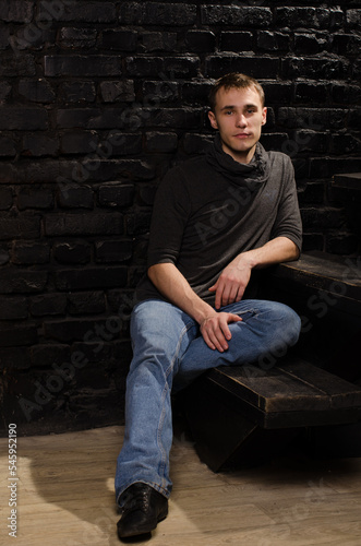 young man in a black sweater sitting on the steps against a brick wall