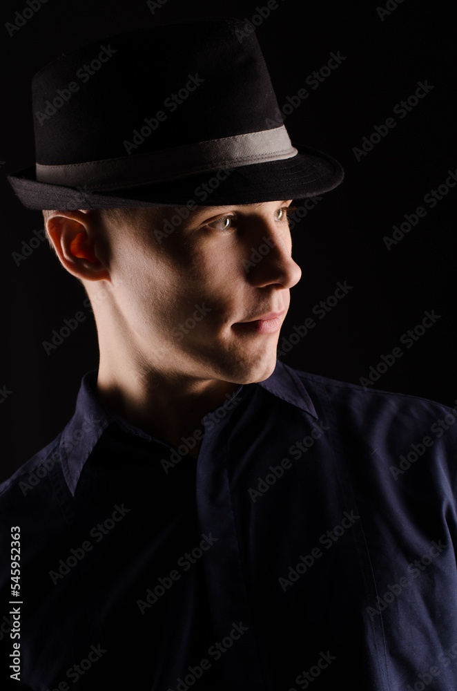 Portrait of a young man in a hat with a ribbon, close-up, on a black background Portrait of a young man in a hat with a ribbon, close-up, on a black background