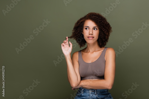 Young african american woman in top touching curly hair isolated on green. © LIGHTFIELD STUDIOS