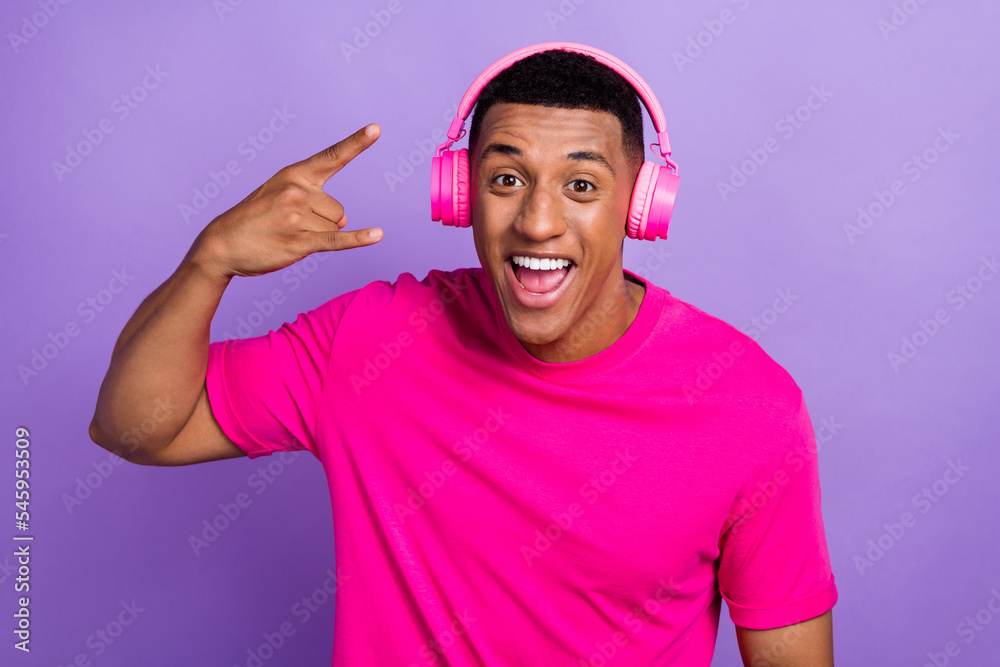 Closeup portrait photo of young rocker music lover listening loud samsung earphones good mood showing fingers symbol isolated on purple color background Closeup portrait photo of young rocker music lover listening loud samsung earphones good mood showing fingers symbol isolated on purple color background
