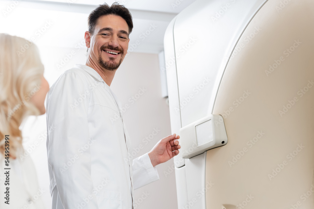 low angle view of smiling radiologist looking at blurred woman near computed tomography machine.