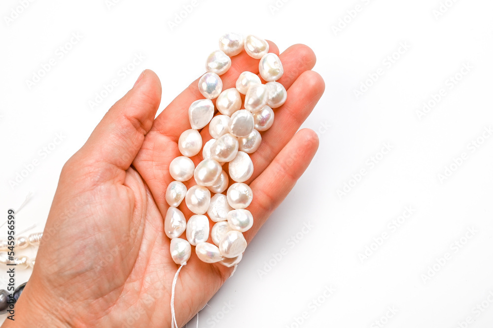 Close-Up of woman hand with string of white baroque pearls isolated on white. Cropped hand holding pearls Close-Up of woman hand with string of white baroque pearls isolated on white. Cropped hand holding pearls