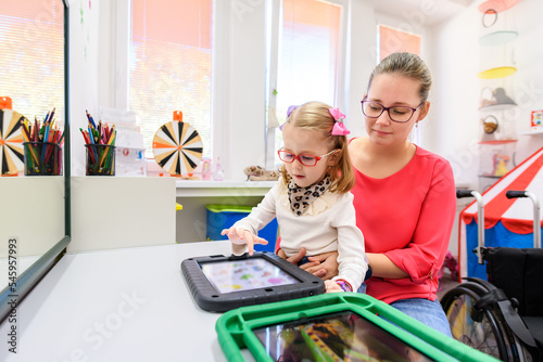 Non-verbal girl living with cerebral palsy, learning to use digital tablet device to communicate. People who have difficulty developing language or using speech use speech-generating devices.