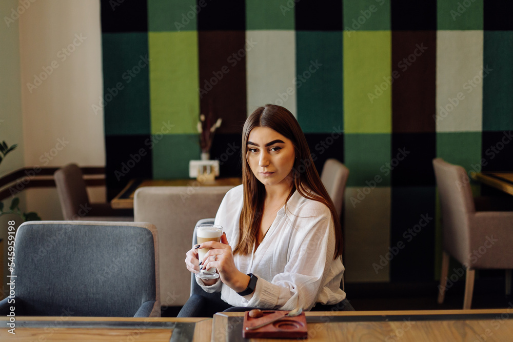 Portrait of beautiful girl, drinking hot tea or coffee in a cafe with her cell mobile phone. Portrait of beautiful girl, drinking hot tea or coffee in a cafe with her cell mobile phone.