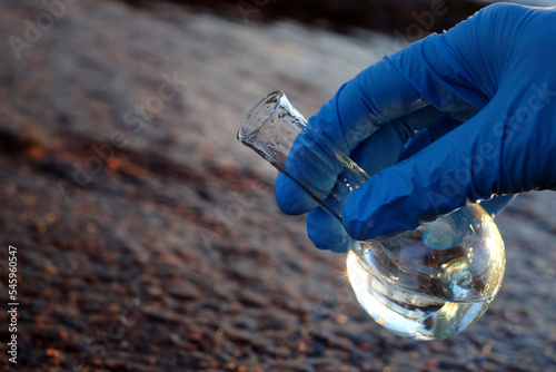 Hand in glove holding water sample for analysis on dark natural background. Ecology concept. Copy space