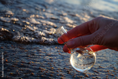Hand holding water sample for analiysis from the sea, sunlight. Ecology concept, with copy space