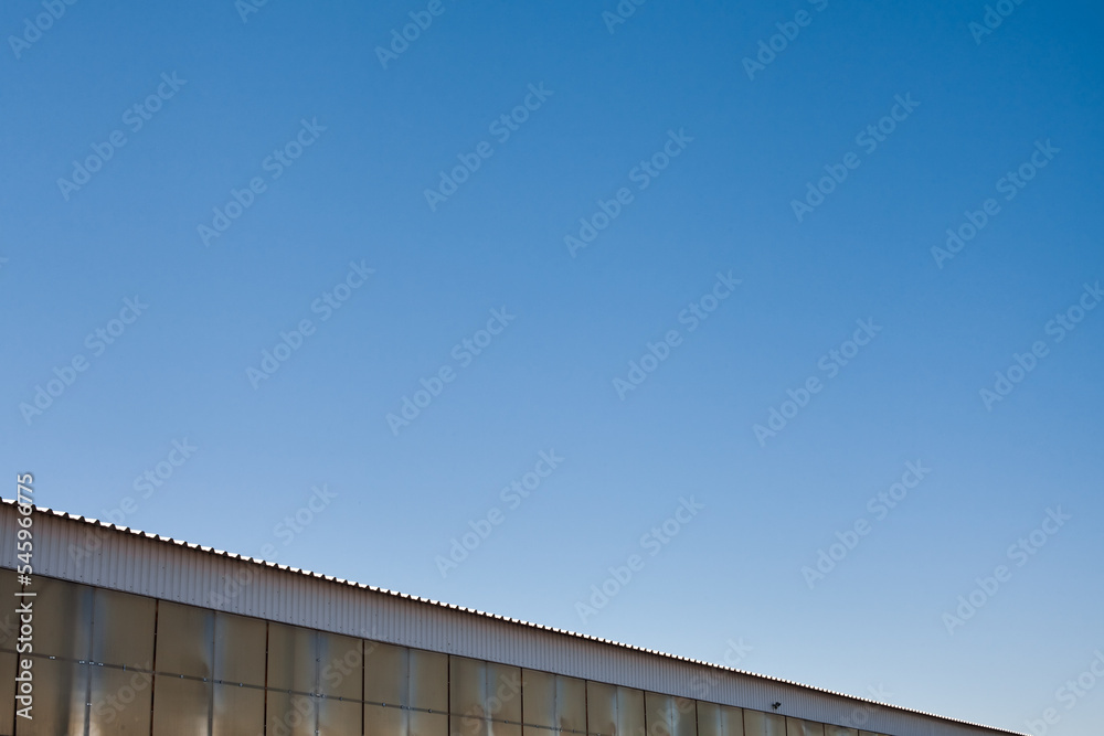 The upper part of an industrial building against the backdrop of a blue clear sky during the day. Background image for your design or illustrations.