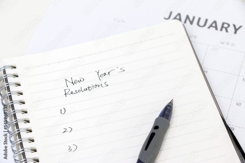 Writing new year’s resolutions, list on notepad with ballpoint pen, January calendar in background, selective focus. Setting goals for the new year. Writing new year’s resolutions, list on notepad with ballpoint pen, January calendar in background, selective focus. Setting goals for the new year.