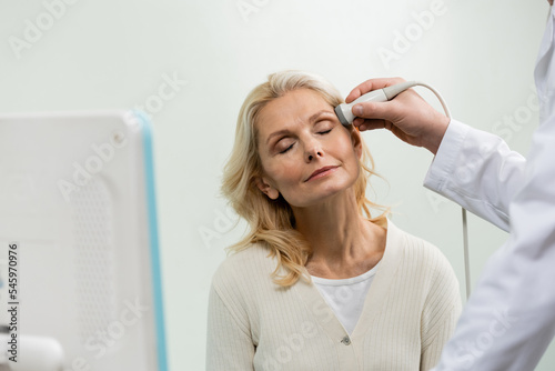 blonde woman with closed eyes near physician doing head ultrasound.