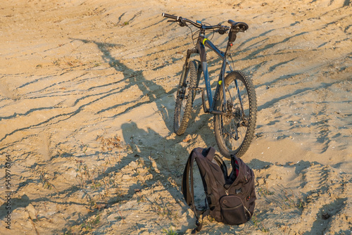 A mountain bike is standing on the sand, and a black backpack is lying next to it