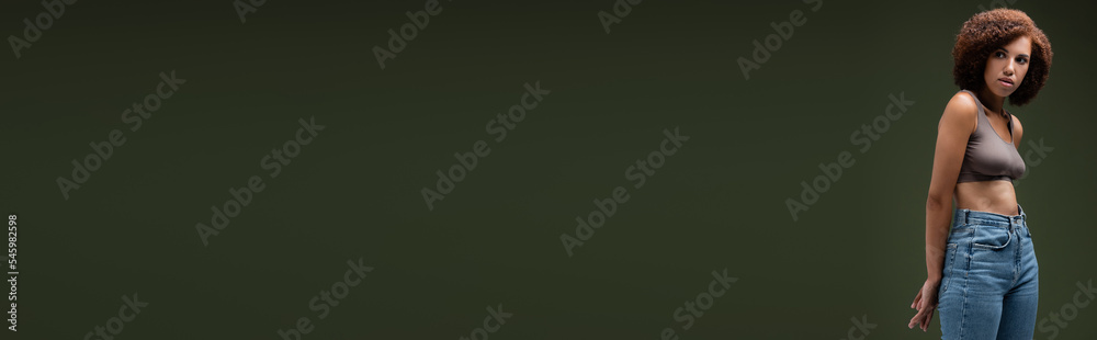 Pretty african american woman in top and jeans looking away isolated on dark green, banner. Pretty african american woman in top and jeans looking away isolated on dark green, banner.