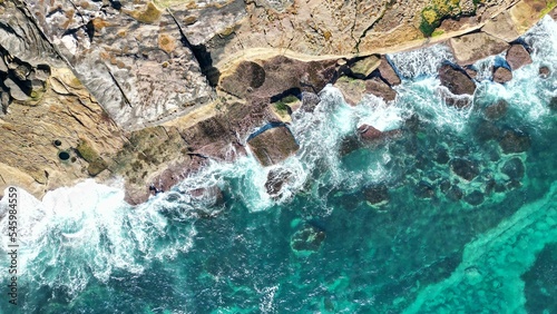 Aerial view of aquamarine waves hitting a rocky shore
