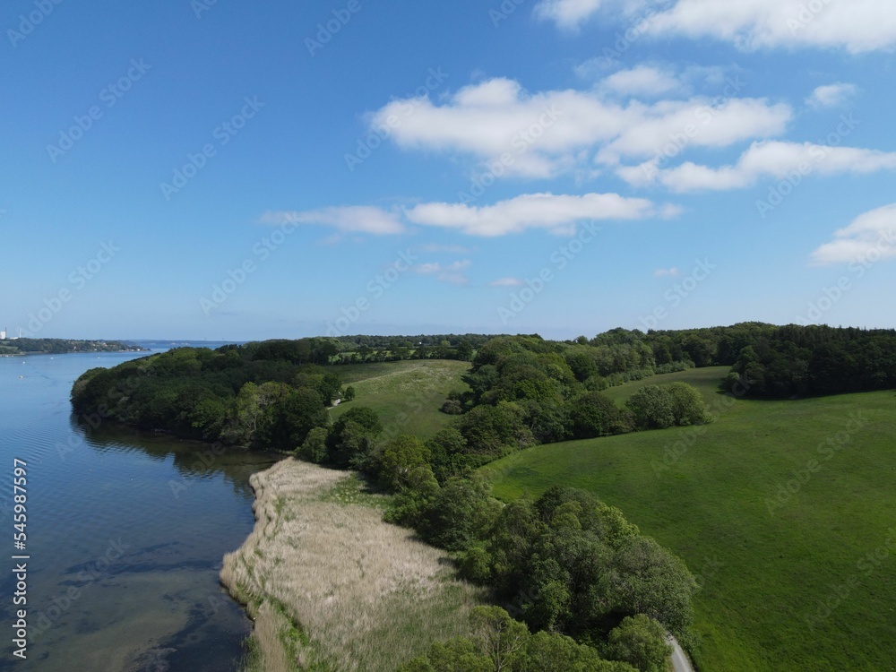 Obraz premium Aerial view of a calm river with green trees and a cloudy blue sky