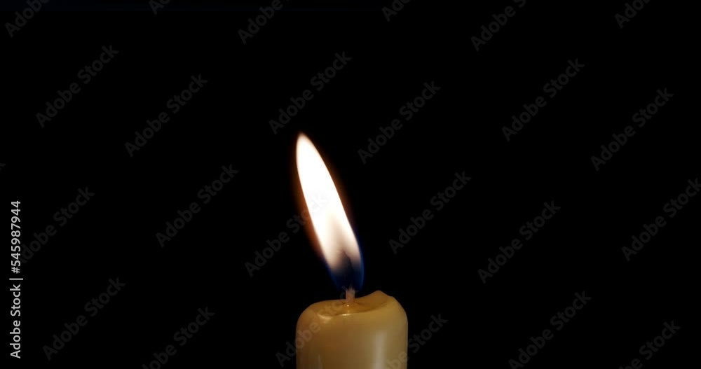 A single white candle burning. Isolated candle slow motion burning with dark background. White paraffin candle with yellow shades burns on a black background. Slow motion. A single white candle burning. Isolated candle slow motion burning with dark background. White paraffin candle with yellow shades burns on a black background. Slow motion.