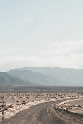 Vertical shot of a narrow road between the desert with hills in the background