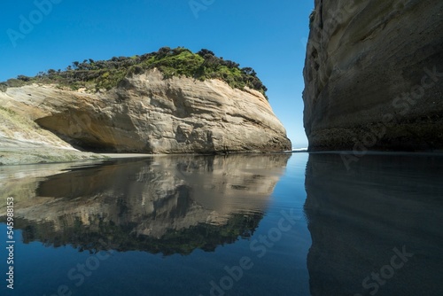 View to Wharariki Beach with huge cliff with greenery reflected in water, Collingwood, New Zealand