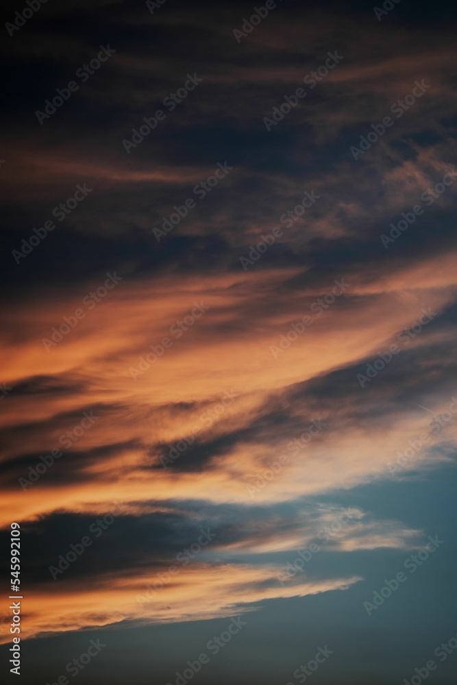 Vertical shot of an orange cloudscape view in a dark sky at sunset