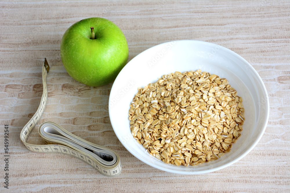 oat flakes in the bowl with green apple and metre on beige background - obrazy, fototapety, plakaty 