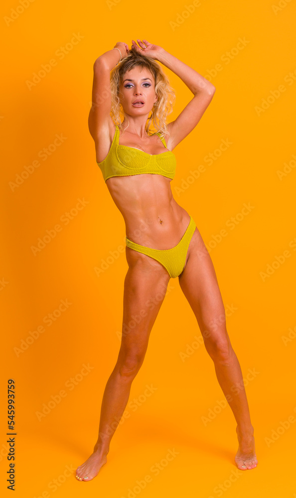 Slim athletic woman posing in a swimsuit on a yellow background. Sport, fitness, diet concept Slim athletic woman posing in a swimsuit on a yellow background. Sport, fitness, diet concept