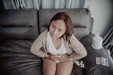 Asian sick woman sit on the sofa stay at home,The woman felt bad, wanted to lie down and rest,stomach ache,menstrual pain