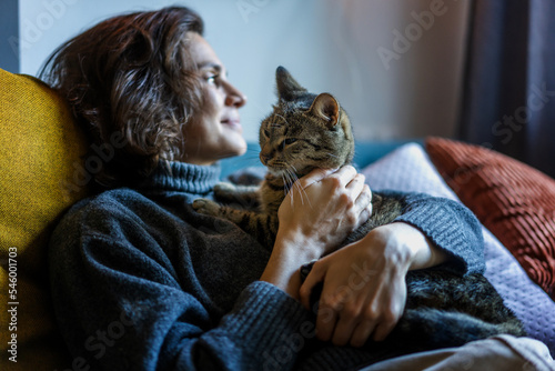 Obraz na płótnie Cheerful smiling young woman in a warm sweater resting at home with a gray cat in her arms w salonie