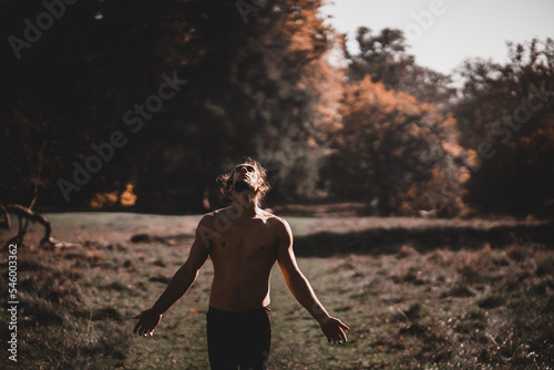 Spanish man with open arms shirtless looking upwards in a forest