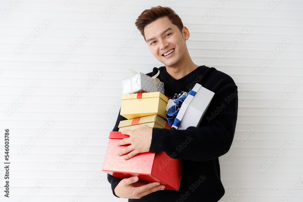 Portrait of a smiling Asian young man holding many gifts box on wall white background Portrait of a smiling Asian young man holding many gifts box on wall white background