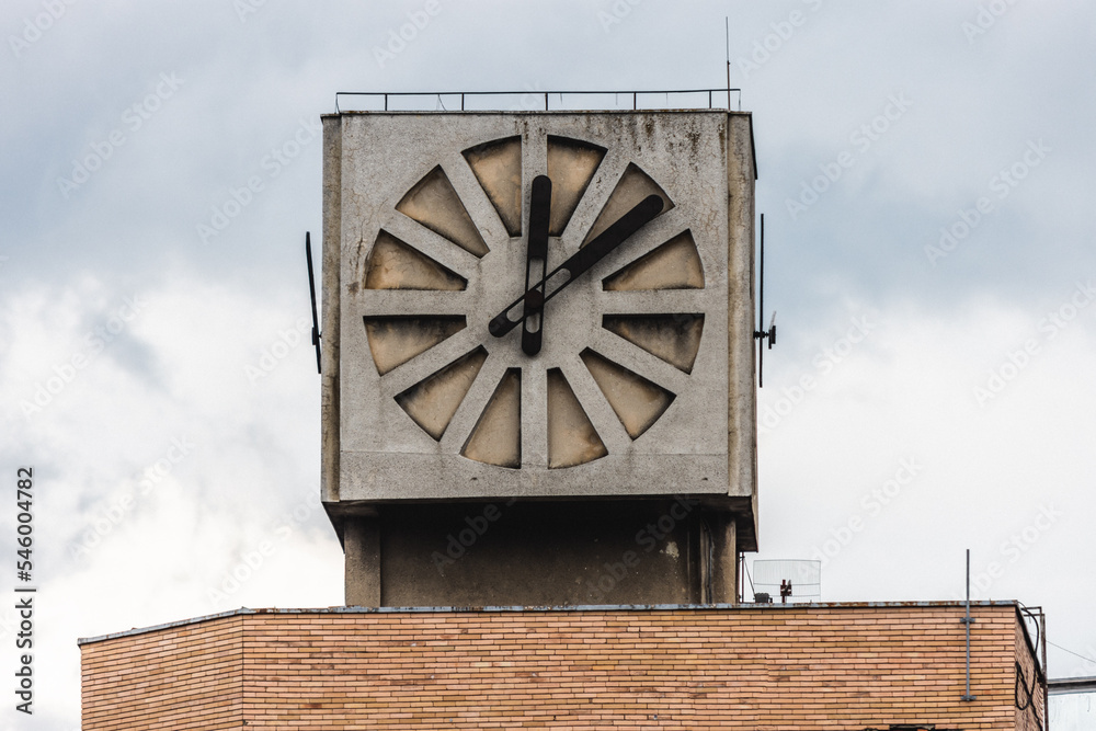 Old cube clock on the roof of a communist construction since communist age in Romania against a bad weather cloudy sky