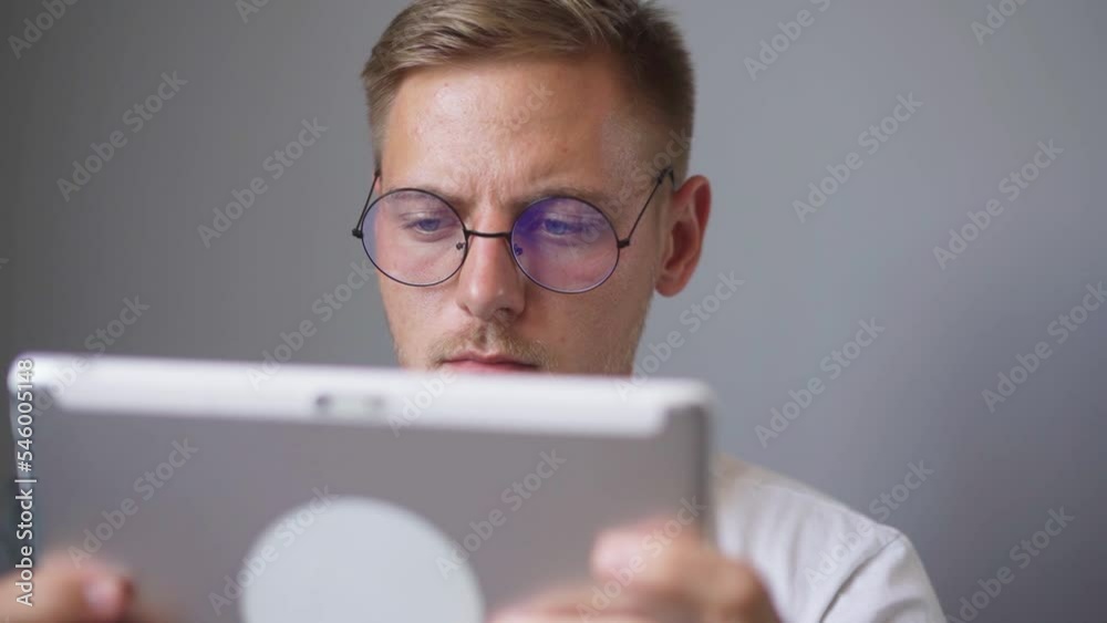 A man with glasses is watching a tablet at home. A man with glasses is watching a tablet at home.
