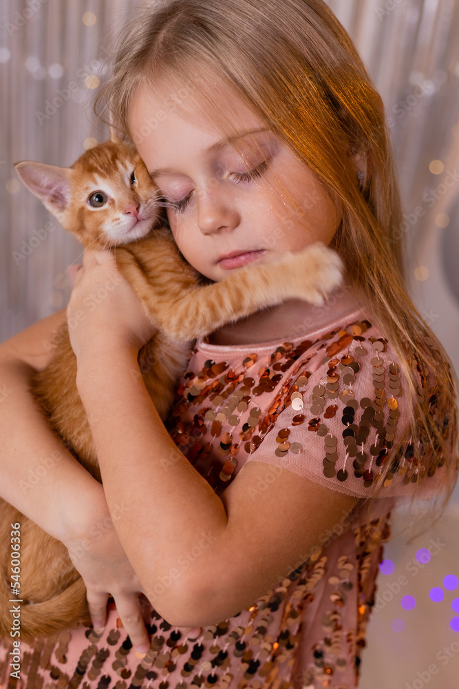 a little princess girl in an elegant dress holds a red kitten in her hands. The symbol of the year is a cat. Children and pets. The concept of the New Year a little princess girl in an elegant dress holds a red kitten in her hands. The symbol of the year is a cat. Children and pets. The concept of the New Year